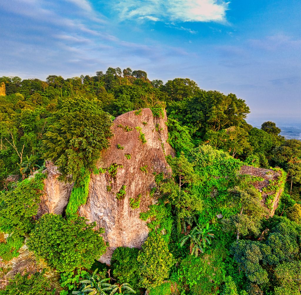 Breathtaking scenery of massive rocky cliff covered with fresh lush green tropical vegetation against cloudy blue sky