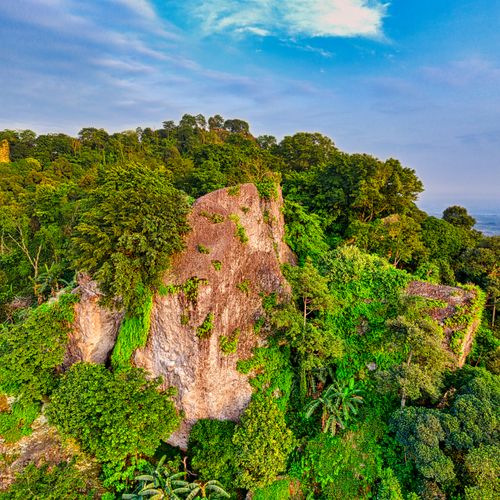 Breathtaking scenery of massive rocky cliff covered with fresh lush green tropical vegetation against cloudy blue sky