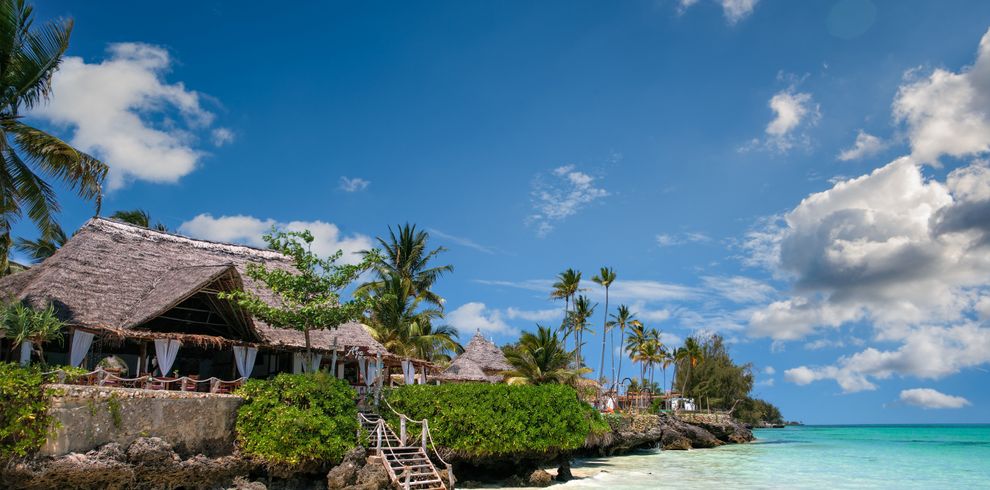 Idyllic beachfront scene in Zanzibar with palm trees, turquoise sea, and a traditional villa.