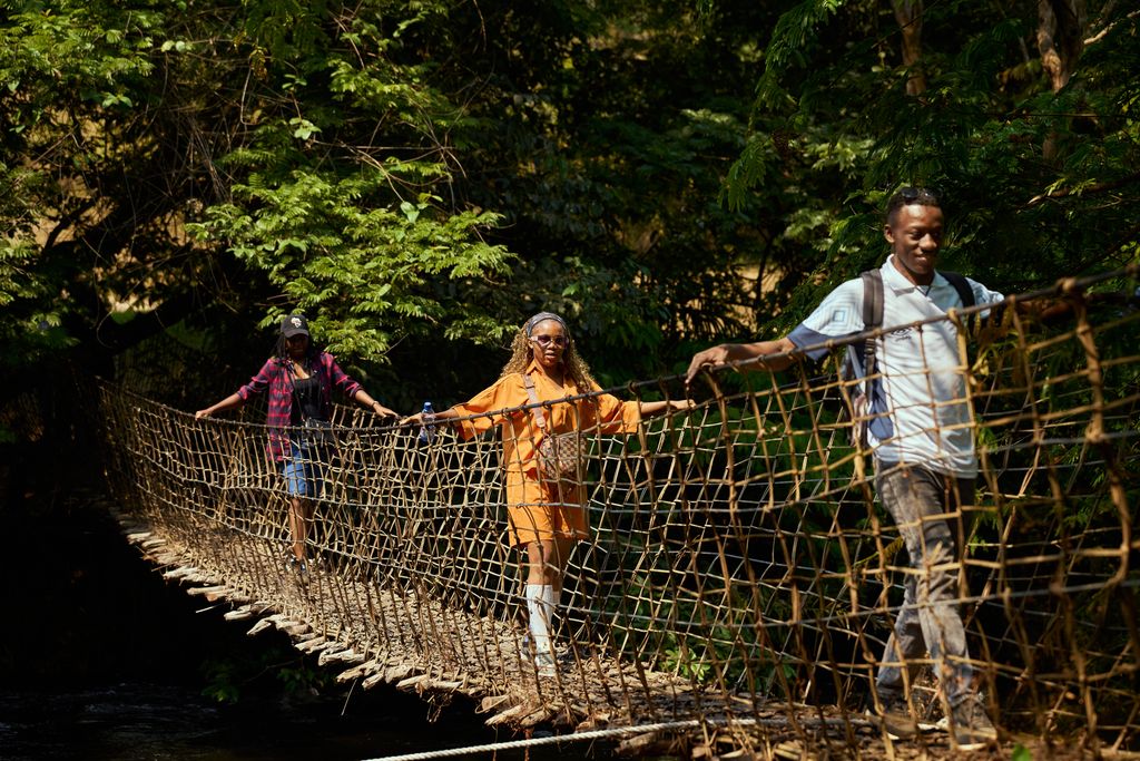 Three adults crossing a rope bridge surrounded by lush greenery.