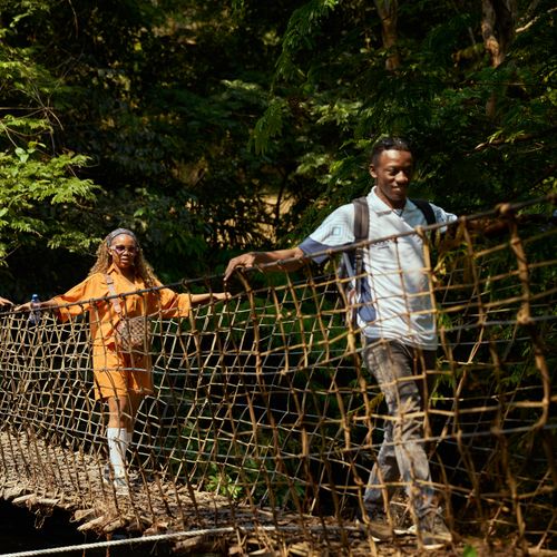 Three adults crossing a rope bridge surrounded by lush greenery.