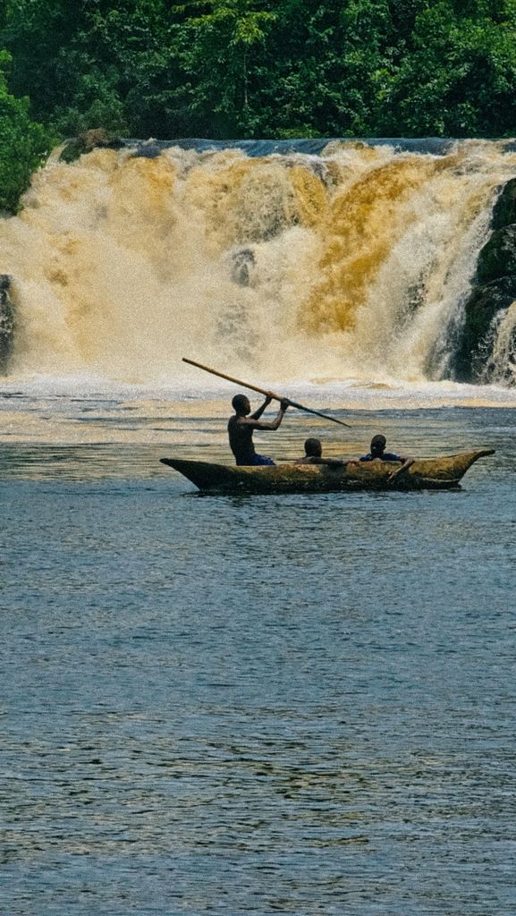 Three people canoeing near a powerful waterfall amidst lush greenery.