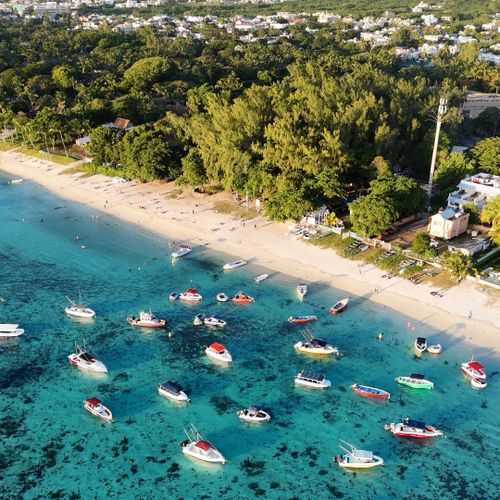 Aerial photo of vibrant boats anchored near the sandy Mauritius coastline, surrounded by lush greenery.