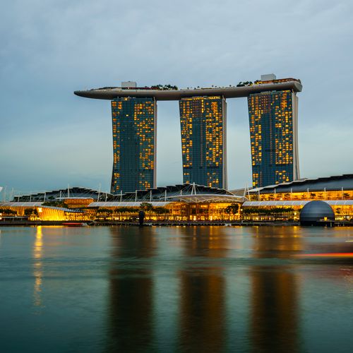 Marina Bay Sands illuminated at sunset in Singapore, reflecting on calm waters.